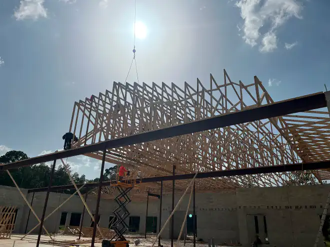 Crane lifting an engineered truss section over the steel and block structure of a Central Florida commercial building