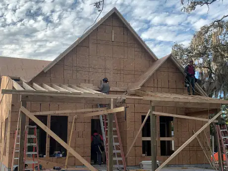 Framing crew working on the sheathed gable roof of a custom home, ladder against the wall