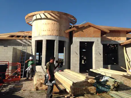 NBJJ crew framing a circular turret on a custom home, lumber staged at the base