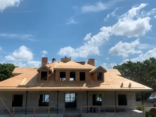 Framing crew working on the ridge of a waterfront estate home, water visible through the porch openings