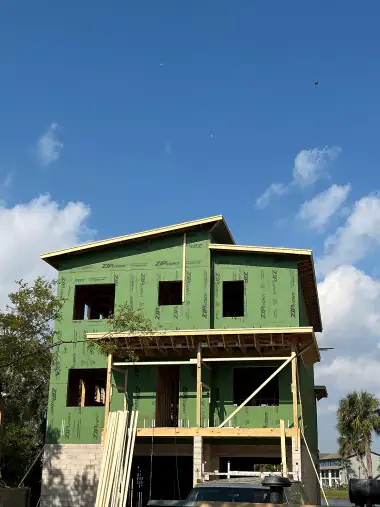 Three-story modern home framed and wrapped in green sheathing, seen from the street