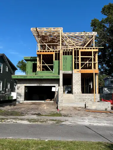 Modern home with green sheathing and a wood roof deck being framed above the garage